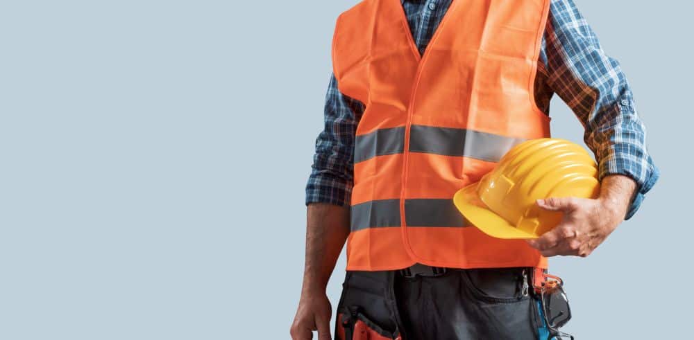 worker wearing reflective clothing holds his hard hat in his hands